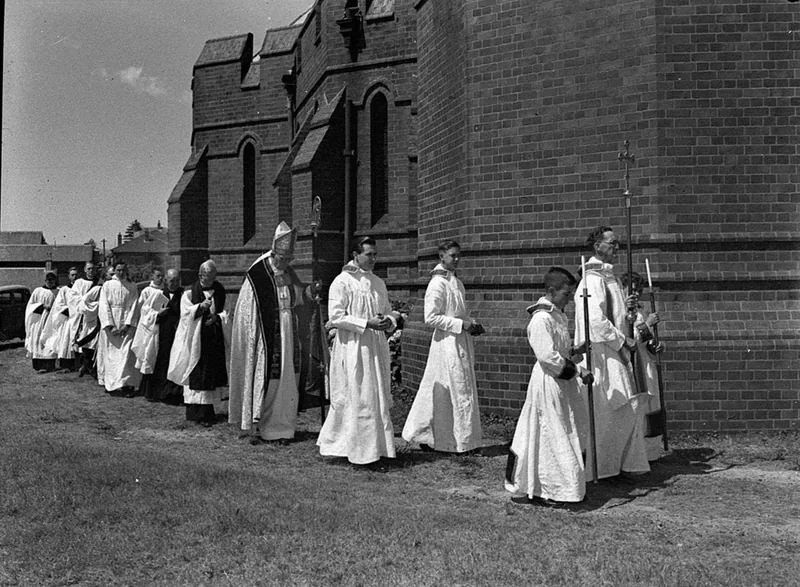 Fotografía de 1952: procesión de clérigos con sobrepelliz junto a la catedral de Newcastle, en Australia, el día de una ordenación