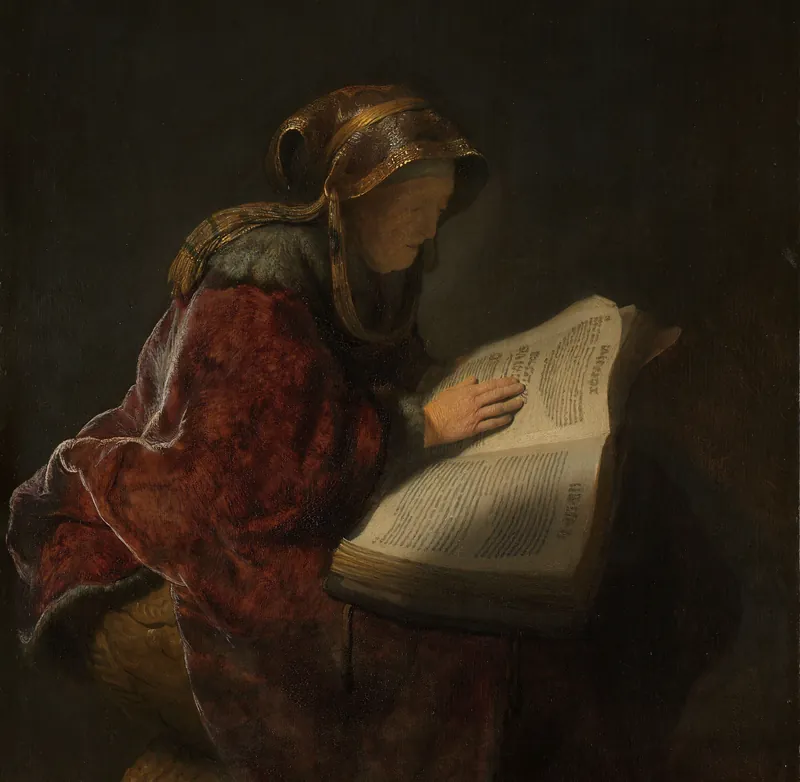 Anciana con manto rojo y tocado dorado que lee un gran libro abierto, con la mano sobre la página, iluminada en la penumbra
